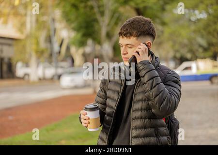 Der Kerl spricht mit seinem Handy, während er durch einen öffentlichen Park geht. Stockfoto