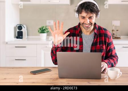 Lächelnder männlicher Student, der sich während eines Videogesprächs zu Hause mit der Hand winkte Stockfoto