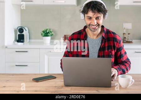 Erwachsener Mann, der Kopfhörer trägt und zu Hause E-Learning mit einem Laptop nutzt Stockfoto