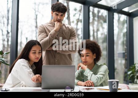 Drei Geschäftskollegen, Die Sich Im Büro Mit Einem Notebook Beschäftigen Stockfoto