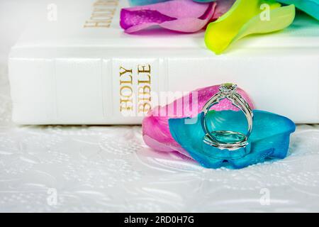 Eheringe auf bunten Rosenblättern mit weißer Heiliger Bibel Stockfoto