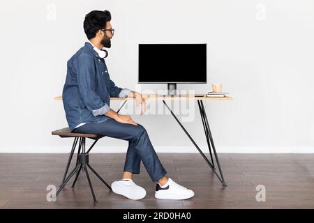 Glücklicher araber, der auf einen Computer mit leerem schwarzem Bildschirm schaut Stockfoto
