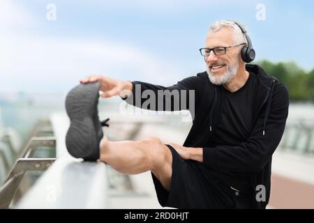 Glücklicher, positiver, erwachsener Sportler, der sich die Beine streckt Stockfoto