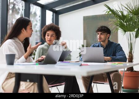 Drei junge, vielfältige Kollegen von Laptops bringen Ideen ins Büro Stockfoto