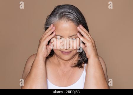 Traurige, ältere, weiße Frau mit grauen Haaren berührt den Kopf und leidet an Migräne Stockfoto