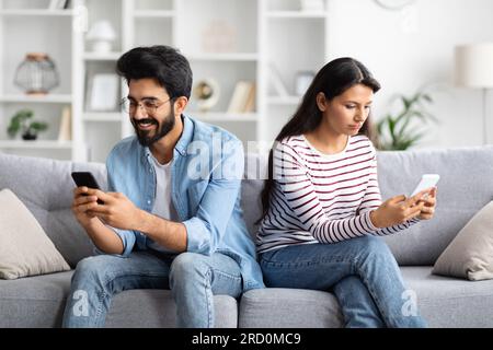 Junge indische Ehefrau und Ehemann, die zu Hause Mobiltelefone benutzen Stockfoto