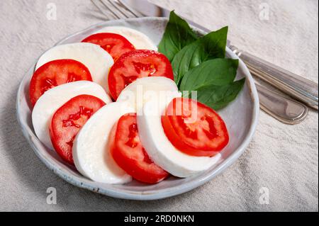 Itaianische vegetarische Speisen, frischer Caprese-Salat mit weißem, weichem italienischen Mozzarella-Käse, roter Tomate und grünem Basilikumöl Stockfoto