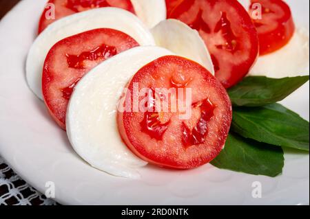 Itaianische vegetarische Speisen, frischer Caprese-Salat mit weißem, weichem italienischen Mozzarella-Käse, roter Tomate und grünem Basilikumöl Stockfoto