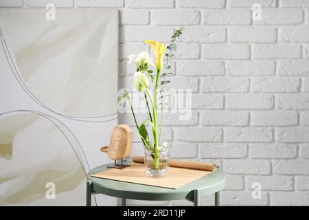 Wunderschönes Ikebana für stilvolles Haus Dekor. Blumenzusammensetzung mit frischen Blumen und Eukalyptuszweig auf dem Kaffeetisch nahe der weißen Backsteinwand Stockfoto