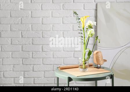 Wunderschönes Ikebana für stilvolles Haus Dekor. Blumenzusammensetzung mit frischen Blumen und Eukalyptuszweig auf dem Kaffeetisch nahe der weißen Backsteinwand, Platz für Stockfoto