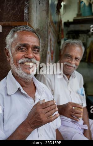 Zwei Freunde genießen Tee in ihrem Marktstand am frühen Morgen entlang der Seitenstraßen von Madurai, Tamil Nadu, Indien, Asien. Stockfoto