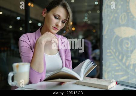 Junge weiße Frau, die in einem Café ein Buch liest Stockfoto