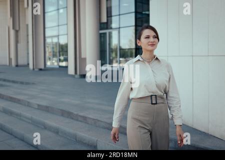 Junge weiße Frau im Geschäftsstil, die zum Mittagessen aus dem Bürogebäude geht Stockfoto
