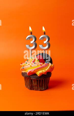 Geburtstagskuchen mit Nummer 33 - Cupcake auf orangefarbenem Hintergrund mit Geburtstagskerzen Stockfoto