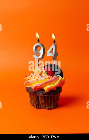 Geburtstagskuchen mit Nummer 94 - Cupcake auf orangefarbenem Hintergrund mit Geburtstagskerzen Stockfoto