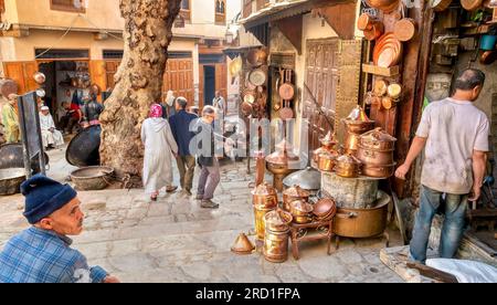 Fez, Marokko - 31. Oktober 2015. Das tägliche Leben im Souk der Stadt, wo Fußgänger an einer Auslage mit Kochgeschirr aus Kupfer vorbeilaufen. Stockfoto