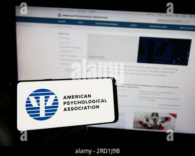 Person, die ein Smartphone mit dem Logo der American Psychological Association (APA) auf dem Bildschirm vor der Website hält. Konzentrieren Sie sich auf das Display des Telefons. Stockfoto