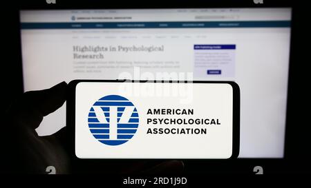 Person, die ein Mobiltelefon mit dem Logo der American Psychological Association (APA) auf dem Bildschirm vor der Webseite hält. Konzentrieren Sie sich auf das Display des Telefons. Stockfoto