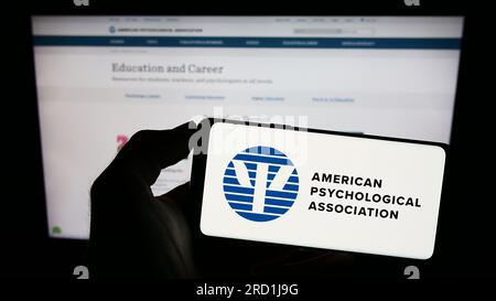 Person, die ein Mobiltelefon mit dem Logo der American Psychological Association (APA) auf dem Bildschirm vor der Webseite hält. Konzentrieren Sie sich auf das Display des Telefons. Stockfoto