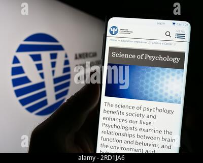 Person, die ein Mobiltelefon mit einer Webseite der American Psychological Association (APA) auf dem Bildschirm vor dem Logo hält. Konzentrieren Sie sich auf die Mitte des Telefondisplays. Stockfoto