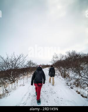 Zwei Frauen versammelten sich vom extrem kalten Spaziergang mit Schneeschuhen und Steigeisen auf einem verschneiten und gefrorenen Pfad in einigen isländischen Bergen in Richtung Wat Stockfoto