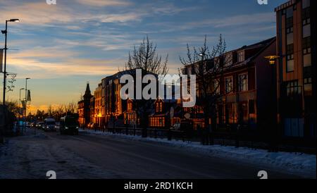 Fassade typischer Reykjavik Häuser beleuchtet von den letzten Strahlen der Abendsonne reflektiert das orange und goldene Licht mit der verschneiten Straße und einem Stockfoto