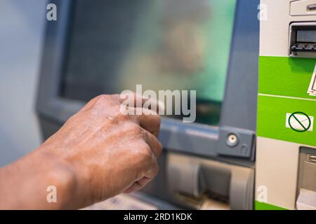 Nahaufnahme männlicher Hände mit Smartphone während des Tippens am Geldautomaten. Ein Mann, der auf dem Schirm eines Geldautomaten reinkommt. Finanzsystem. Moderne Technologie Stockfoto