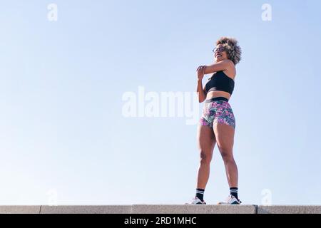 Eine Frau in Sportbekleidung, die fröhlich lächelt und Arme streckt Stockfoto