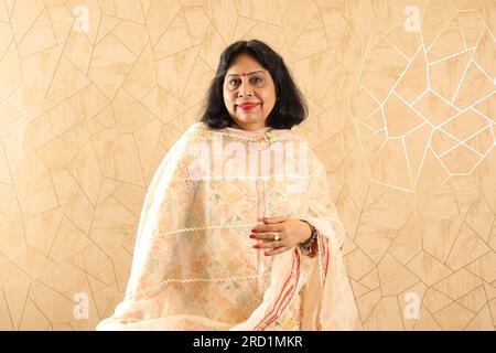 Alte Indianerin, die mit der Wand steht. Weiße Wand. Wunderschönes glückliches Porträt von Großmutter, die im neu eingerichteten Wohnzimmer an der Wand steht. Stockfoto