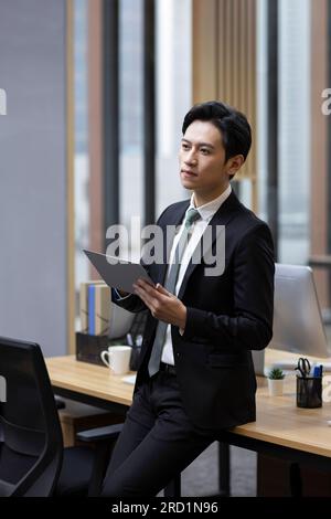 Junger chinesischer Geschäftsmann, der im Büro ein Tablet benutzt Stockfoto