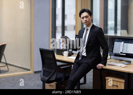 Junger chinesischer Geschäftsmann, der im Büro ein Tablet benutzt Stockfoto