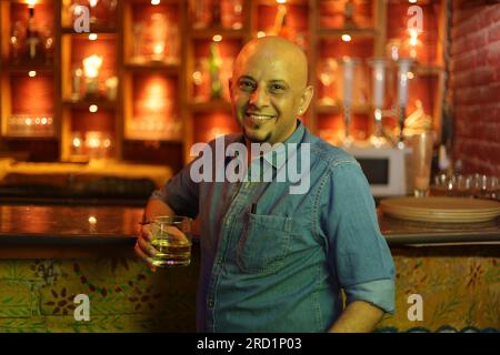 Dramatische Aufnahme eines jungen und attraktiven, glatzköpfigen Kerls, der an der Theke steht. Genießen Sie die Inneneinrichtung des City Clubs im Nachtklub mit einem Glas Whiskey Stockfoto