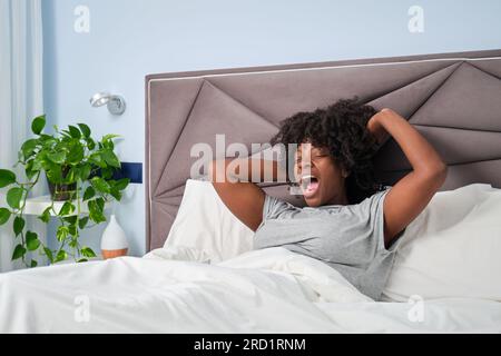 Glückliche afrikanische lächelnde Frau, die morgens gähnt und sich auf dem Bett streckt. Stockfoto