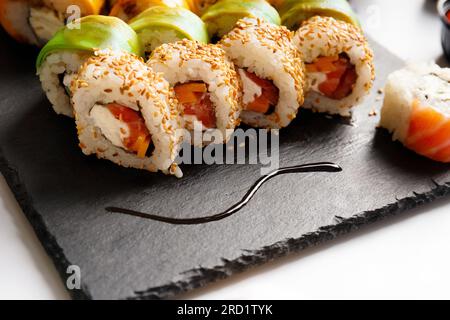 Legen Sie die Rolle mit Lachs, Avocado, Garnelen und Aal auf einem Steinbrett auf grauem Hintergrund, Nahaufnahme Stockfoto