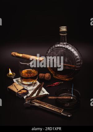 Hochwertige Zigarren mit Cognac, Cutter, 100-Dollar-Papier, Aschenbecher, heller Vintage-Kerze und rotem, heißem Pfeffer auf schwarzem Hintergrund Stockfoto