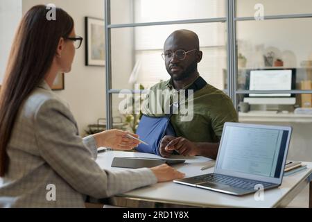 Ein Afroamerikaner mit Verletzten, der sich mit einem Versicherungsagenten im Büro trifft Stockfoto