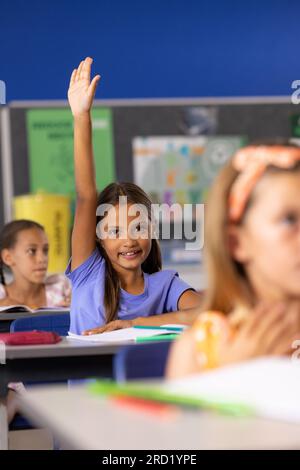 Porträt von fröhlichen, vielfältigen Schulmädchen, die im Klassenzimmer die Hand heben Stockfoto