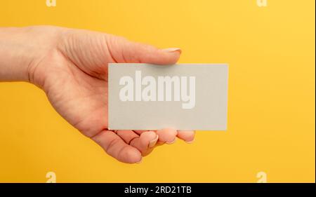 Weiße Visitenkarte mit Kopierbereich in weiblicher Hand auf gelbem Hintergrund. Für Kontaktinformationen und Präsentation ist kein Identitätskennzeichen angegeben Stockfoto