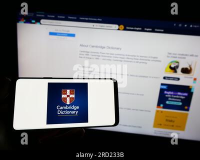 Person, die ein Mobiltelefon mit dem Logo des Cambridge Dictionary auf dem Bildschirm vor der Webseite hält. Konzentrieren Sie sich auf das Display des Telefons. Stockfoto