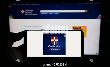 Person, die ein Smartphone mit dem Logo des Cambridge Dictionary auf dem Bildschirm vor der Website hält. Konzentrieren Sie sich auf das Display des Telefons. Stockfoto