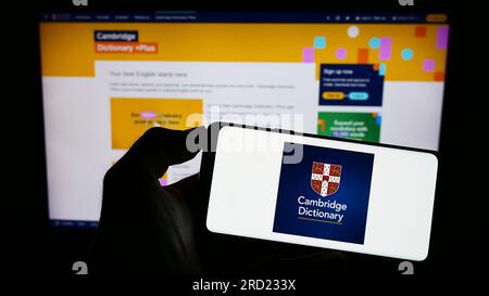 Person, die ein Mobiltelefon mit dem Logo des Cambridge Dictionary auf dem Bildschirm vor der Webseite hält. Konzentrieren Sie sich auf das Display des Telefons. Stockfoto