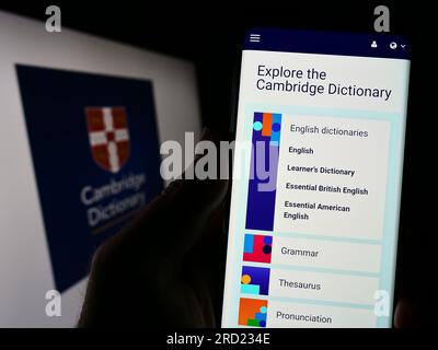 Person, die ein Mobiltelefon mit dem Logo des Cambridge Dictionary auf dem Bildschirm vor der Webseite hält. Konzentrieren Sie sich auf die Mitte des Telefondisplays. Stockfoto