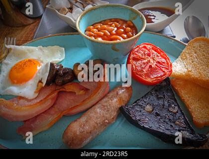 Britisches traditionelles warmes Frühstück, Spiegelei, Speck, Wurst, schwarzer Pudding, Gebratenes Brot, Bohnen, gegrillte Tomaten und Pilze Stockfoto