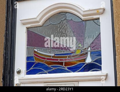 Buntglasscheibe in einer Eingangstür, die Fischerboote und Fischer in einer traditionellen Küstenszene darstellt, Filey, North Yorkshire, England, YO14 9BB Stockfoto