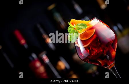 Rotes Sangria-Sommergetränk mit spanischem Rotwein, Pfirsich, Pflaume, Orange, Limette und Eis. Schwarzer Bartheke-Hintergrund, Stahlbarren und Flaschen Stockfoto