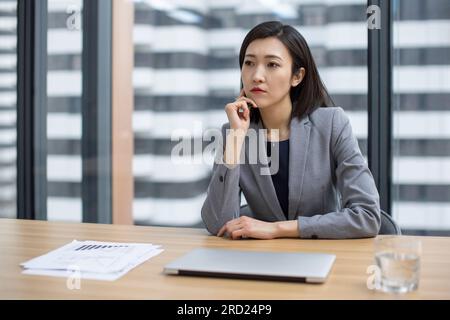 Junge chinesische Geschäftsfrau, die im Konferenzraum denkt Stockfoto
