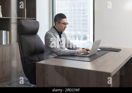 Erfolgreicher chinesischer Geschäftsmann mit Laptop im Büro Stockfoto