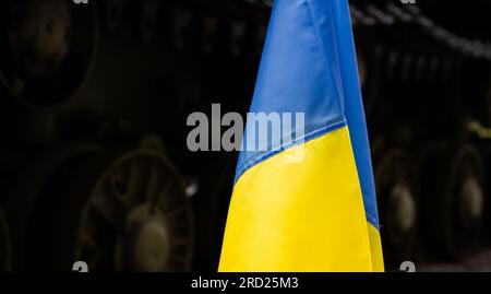 Ukrainische Nationalflagge, mit Kampfpanzer im Hintergrund. Protestmanifestation gegen die russische Invasion, Krieg in der Ukraine. Stockfoto