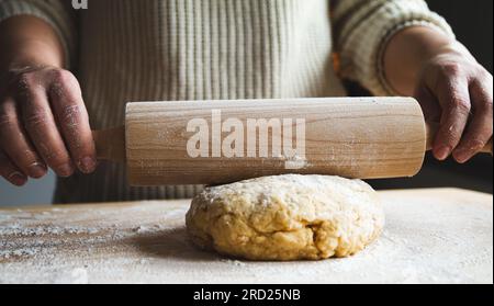 Frau, die eine Rolle spielt und Teig für Pizza, Brot, hausgemachten Kuchen oder Weihnachtskekse zubereitet. Weibliche Hände Rollen Teig mit Zapfen. Stockfoto
