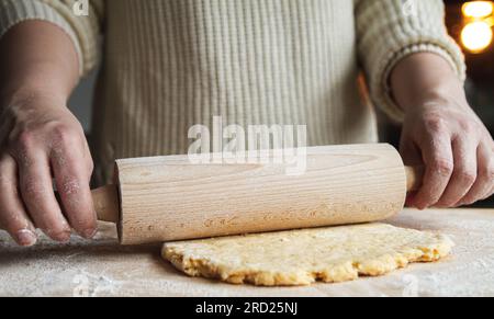 Frau, die eine Rolle spielt und Teig für Pizza, Brot, hausgemachten Kuchen oder Weihnachtskekse zubereitet. Weibliche Hände Rollen Teig mit Zapfen. Stockfoto